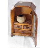 An oak smoker's cabinet, the glazed front door opening to reveal a cavity above two short and one