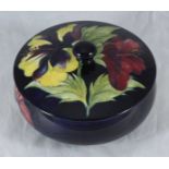 A Moorcroft Hibiscus pattern circular powder pot and cover painted to a dark blue ground,