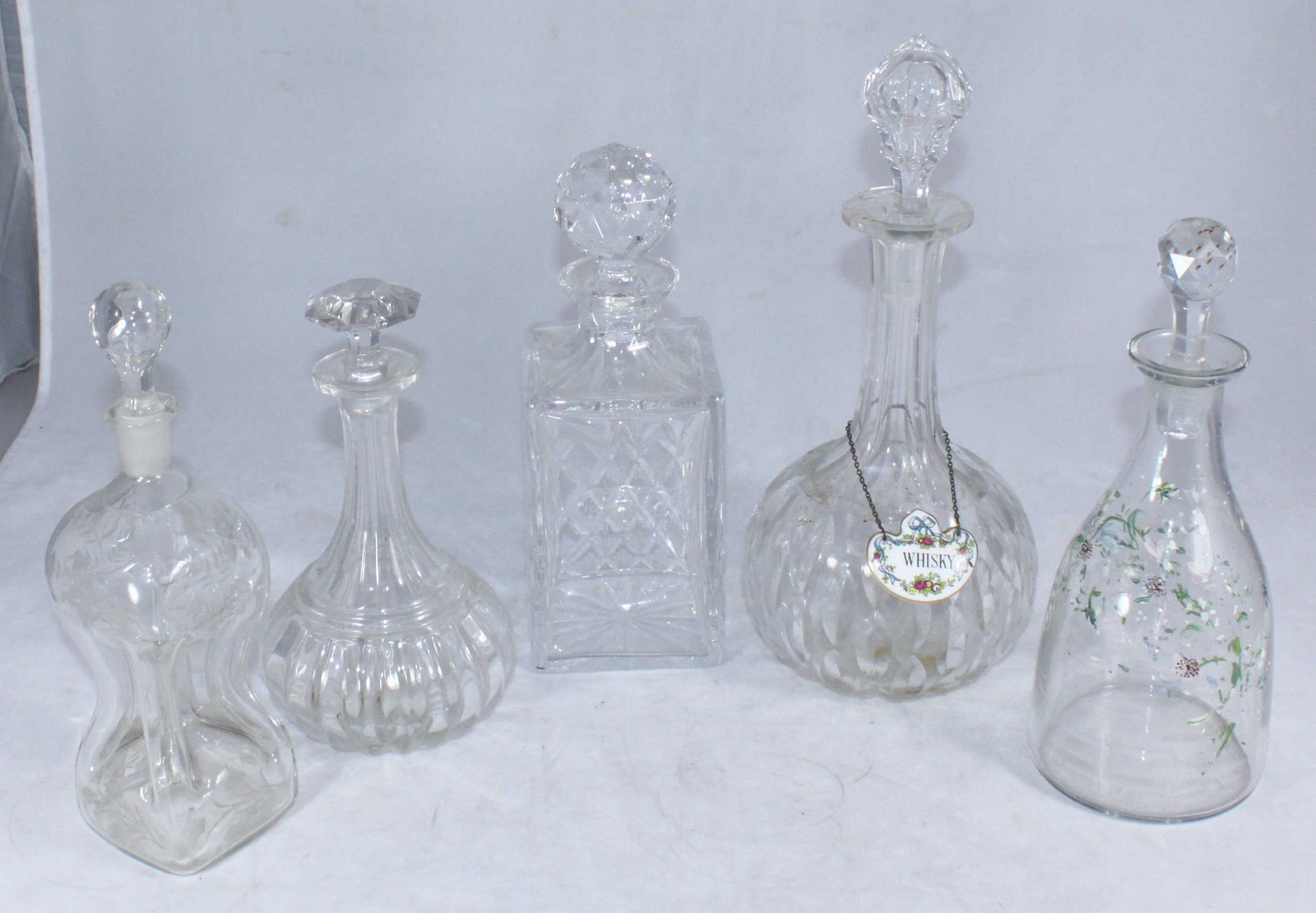 A cruciform decanter and stopper, a floral enamelled decanter and three further decanters with