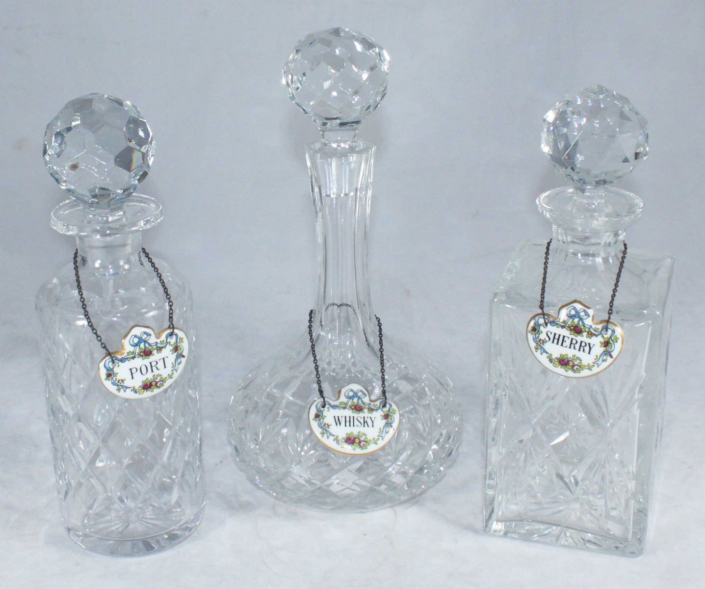 Three assorted glass decanters and stoppers, each with Staffordshire ceramic spirit labels, for