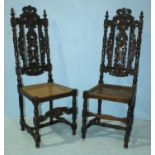 A pair of Gothic style carved oak hall chairs, with caned seats and raised on turned supports