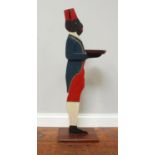 A blackamoor dumb waiter with red hat, blue blazer and red trousers holding circular plate, raised