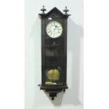 A stained Vienna wall clock the top with two turned finials, above a glass front exposing white dial