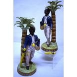A pair of nineteenth century French porcelain figures of black boys standing underneath palm