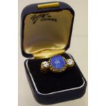 A large oval blue opal ring, flanked by two diamonds, in a carved gold setting, boxed.