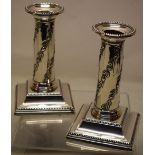 A pair of Edwardian silver dwarf candlesticks, the pillar stems with repousse trailing foliage,