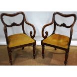A pair of early Victorian mahogany buckle back elbow chairs, with rococo leaf cartouches to the