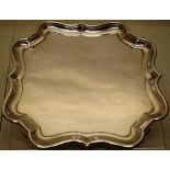 An Edwardian silver salver, having a raised serpentine border, the angled corners on panel feet, 9in