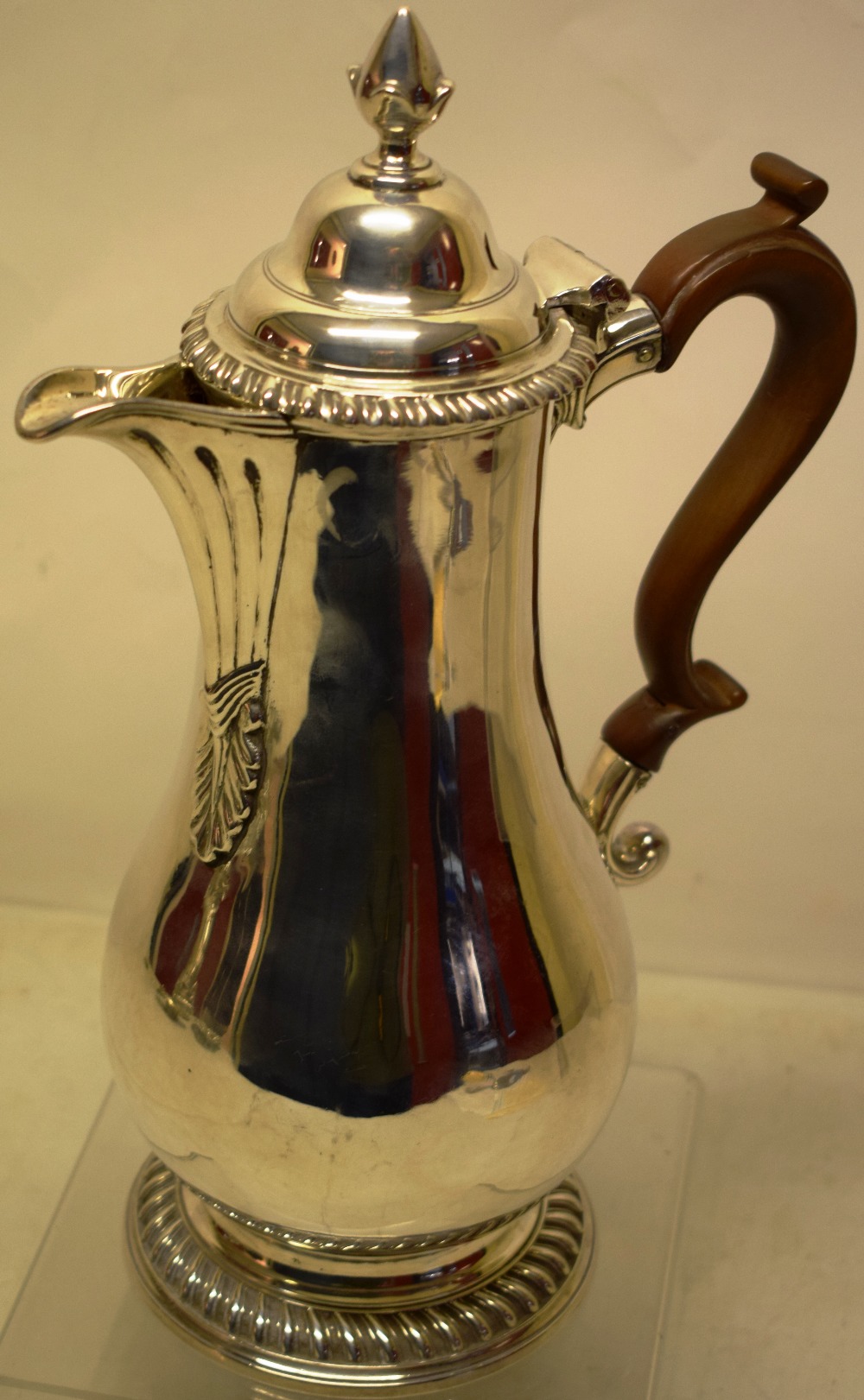 A George III silver baluster jug, having a fluted scroll spout with a leaf pendant, a hinged ogee