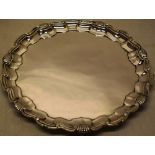 A circular silver salver, the raised moulded border with a shell scroll edge, on three leaf scroll