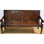 An eighteenth century oak settle, the back with four shaped top fielded panels, the arms on scroll