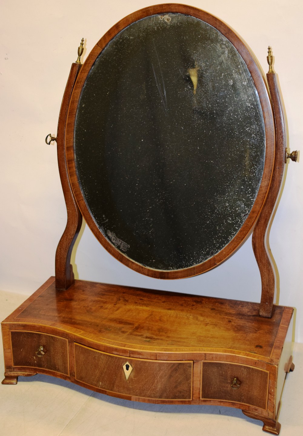 A Sheraton mahogany veneered oval swing toilet mirror, inlaid stringing, with scroll side