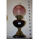 A brass oil lamp having a red reservoir and cranberry glass shade with two wicks.