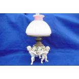 A DRESDEN OIL LAMP WITH CHERUBS AND PINK SHADE