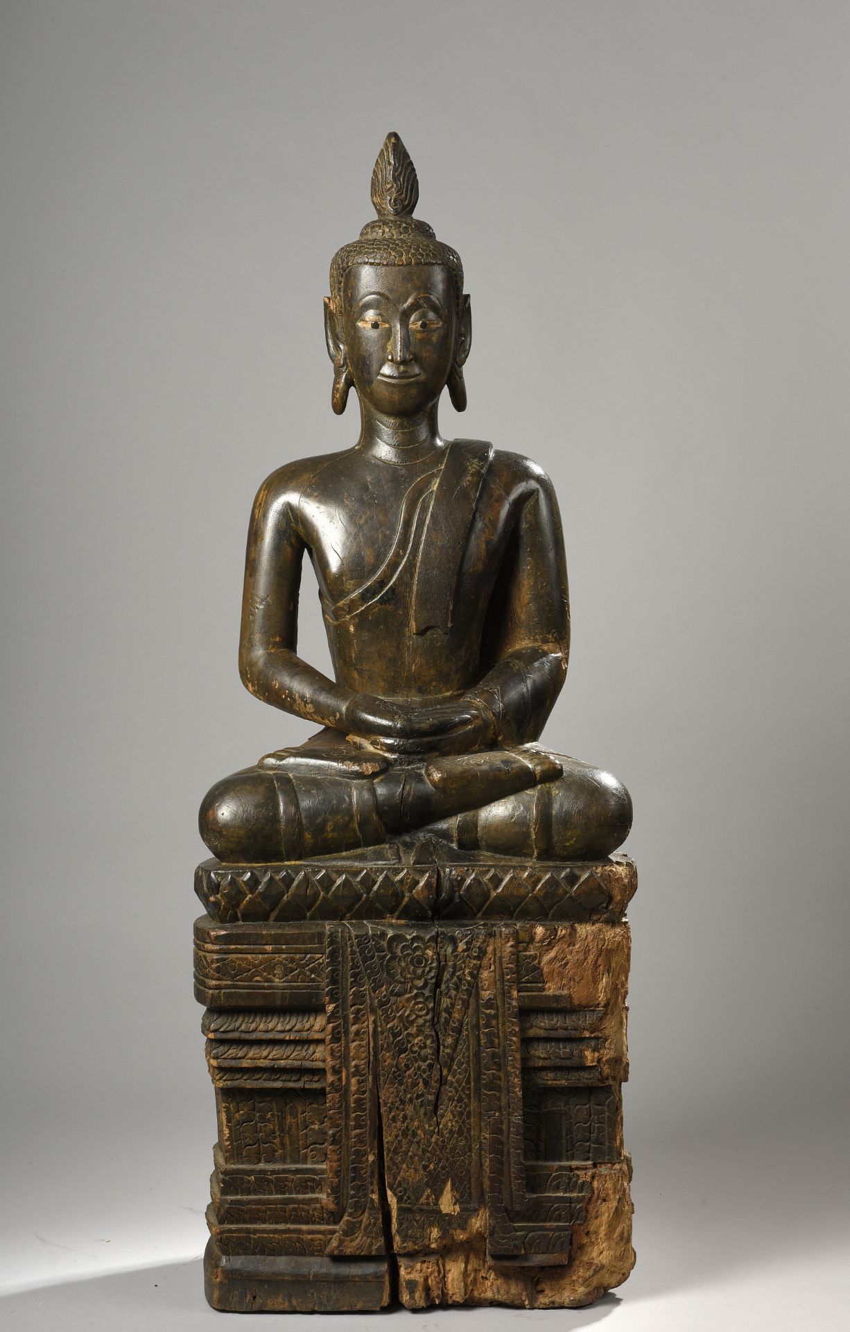 Buddha assis en virasana sur un haut socle à base lotiforme d'où pend une [...]