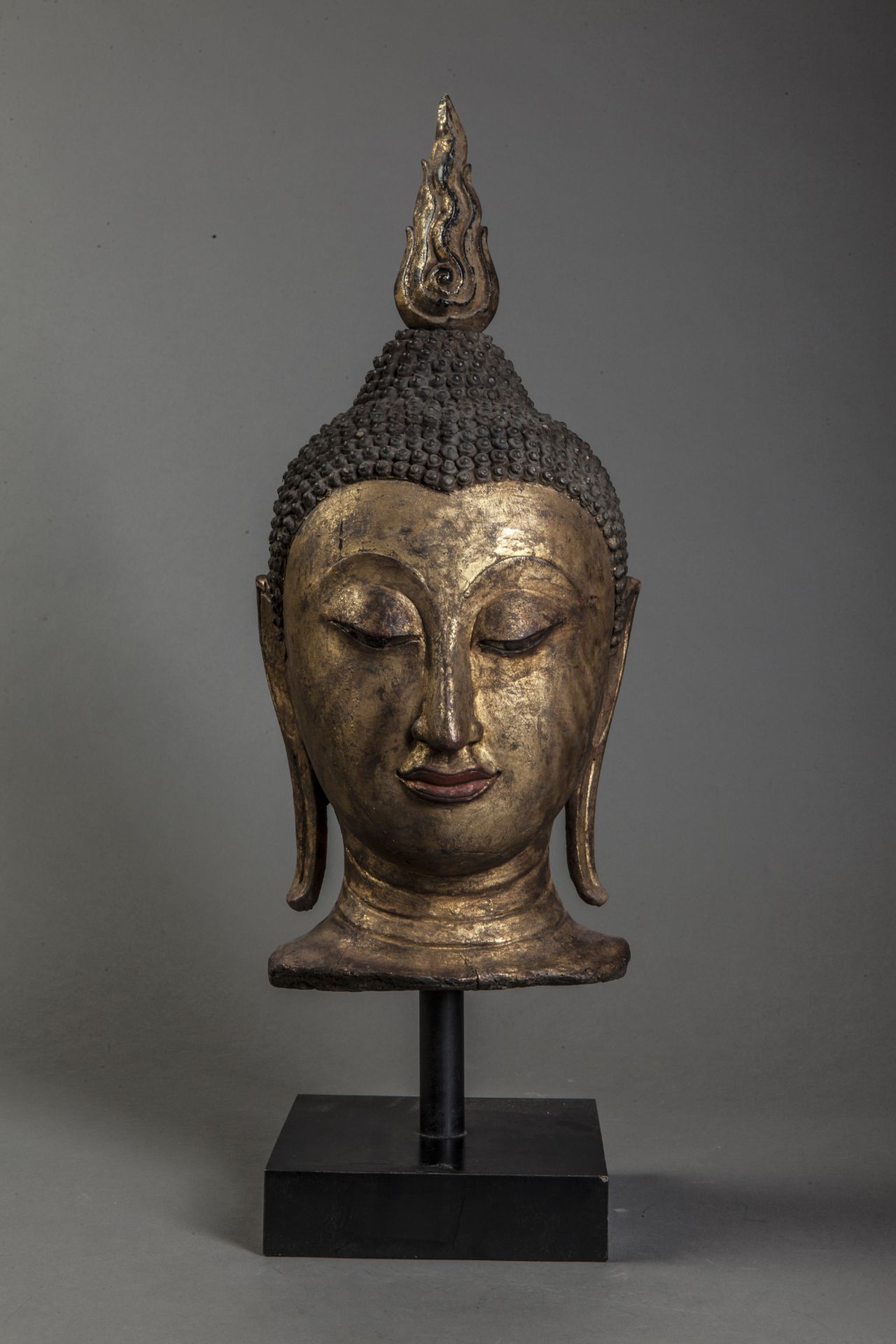 Tête de Buddha coiffée de fines bouclettes surmontée d'un haut rasmi. Bois laqué [...]
