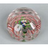 A faceted glass paperweight with a polychrome flower spray under an opaque red and white twist ring,