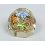 A faceted domed glass paperweight containing four flower sprays issuing from polychrome pebbles,