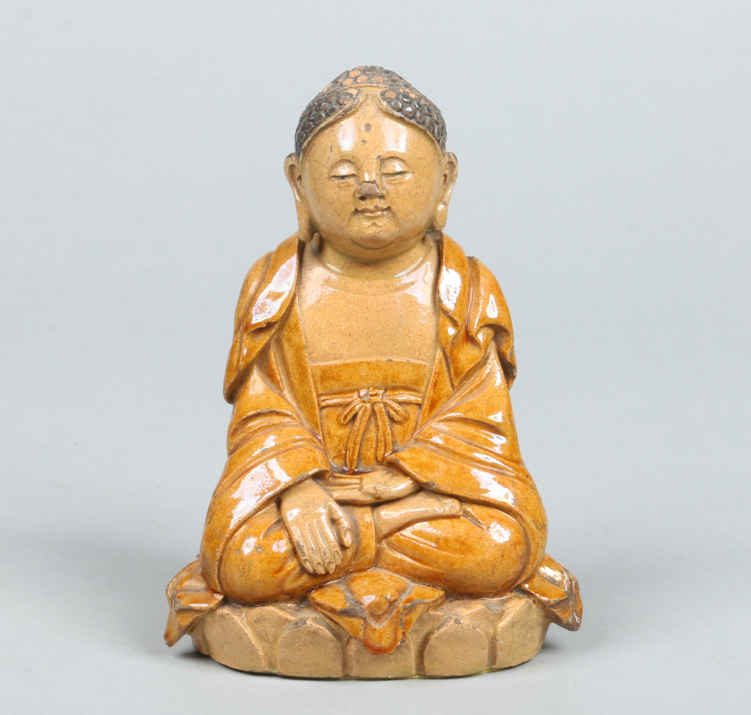 A Chinese earthenware figure of a seated meditating Buddha raised on a lotus plinth and in ochre