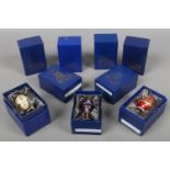 Nine boxed enamelled brass egg shaped trinket boxes on stands.