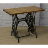 A hardwood occasional table with cast iron Singer treadle sewing machine base.