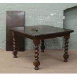 An oak wind out dining table raised on barleytwist supports with winding handle.