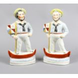 A pair of Staffordshire figures of men in naval attire holding flags and standing in a boat.