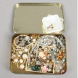 A tin of costume jewellery including clip on earrings, aurora borealis necklace, brooches etc.