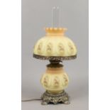 A tablelamp formed as an oil lamp with yellow glass shade and floral decoration.