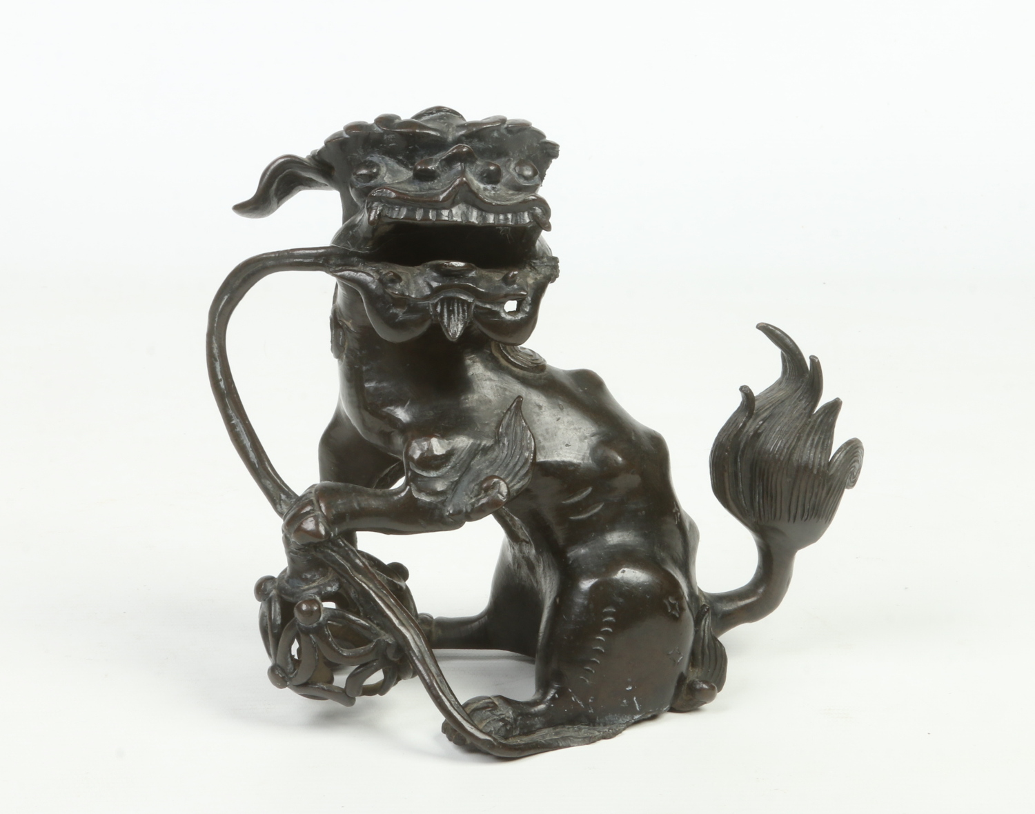 An antique Chinese patinated bronze sculpture of a lion dog guarding a brocade bowl, possibly