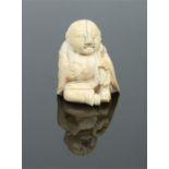 A Japanese Edo period miniature carved ivory figure. Formed as a seated Buddha holding beads and a