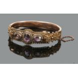 A 9 carat gold bangle with a filigree and openwork panel set with three large ovoid amethysts