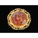 A yellow metal and carved agate roundel brooch. With pierced border and decorated to the centre with