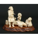 A Japanese Meiji period carved ivory okimono group on wooden plinth. Formed as a seated man