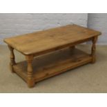 A stained pine two tier coffee table raised on turned supports.