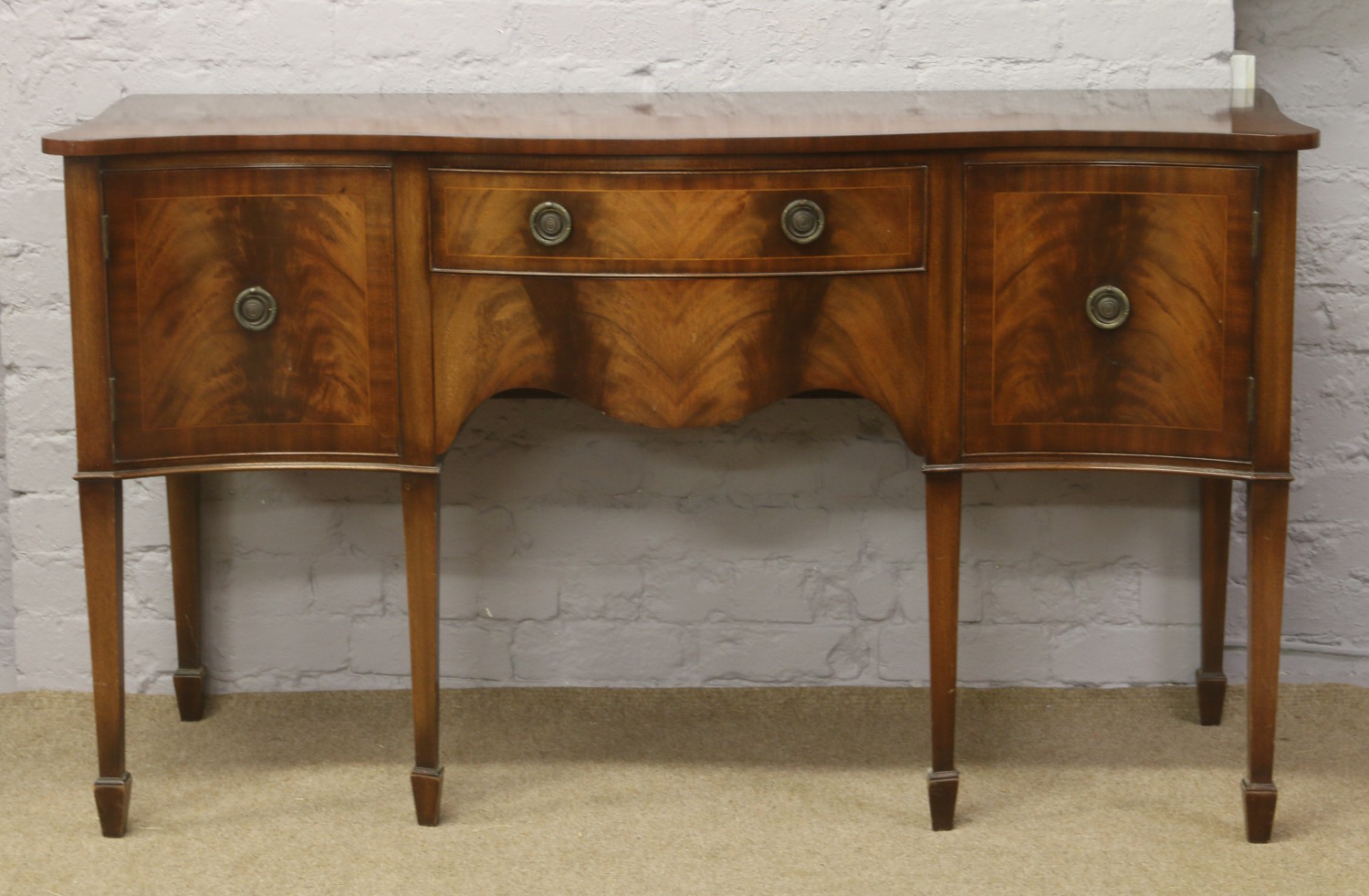 A mahogany serpentine sideboard crossbanded with strung inlay and raised on square tapering