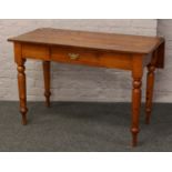 A Victorian pine single drawer drop leaf kitchen table raised on turned supports.