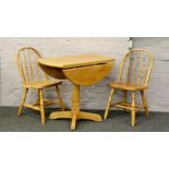 A pine drop leaf dining table and pair of spindle back chairs.