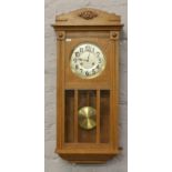 A carved light oak 8 day wall clock with silvered dial, pendulum and key.