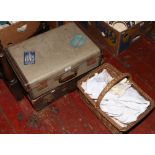 Two vintage suitcases, along with a basket of linen and ladies white leather gloves.