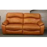 A tan leather two seat reclining sofa.