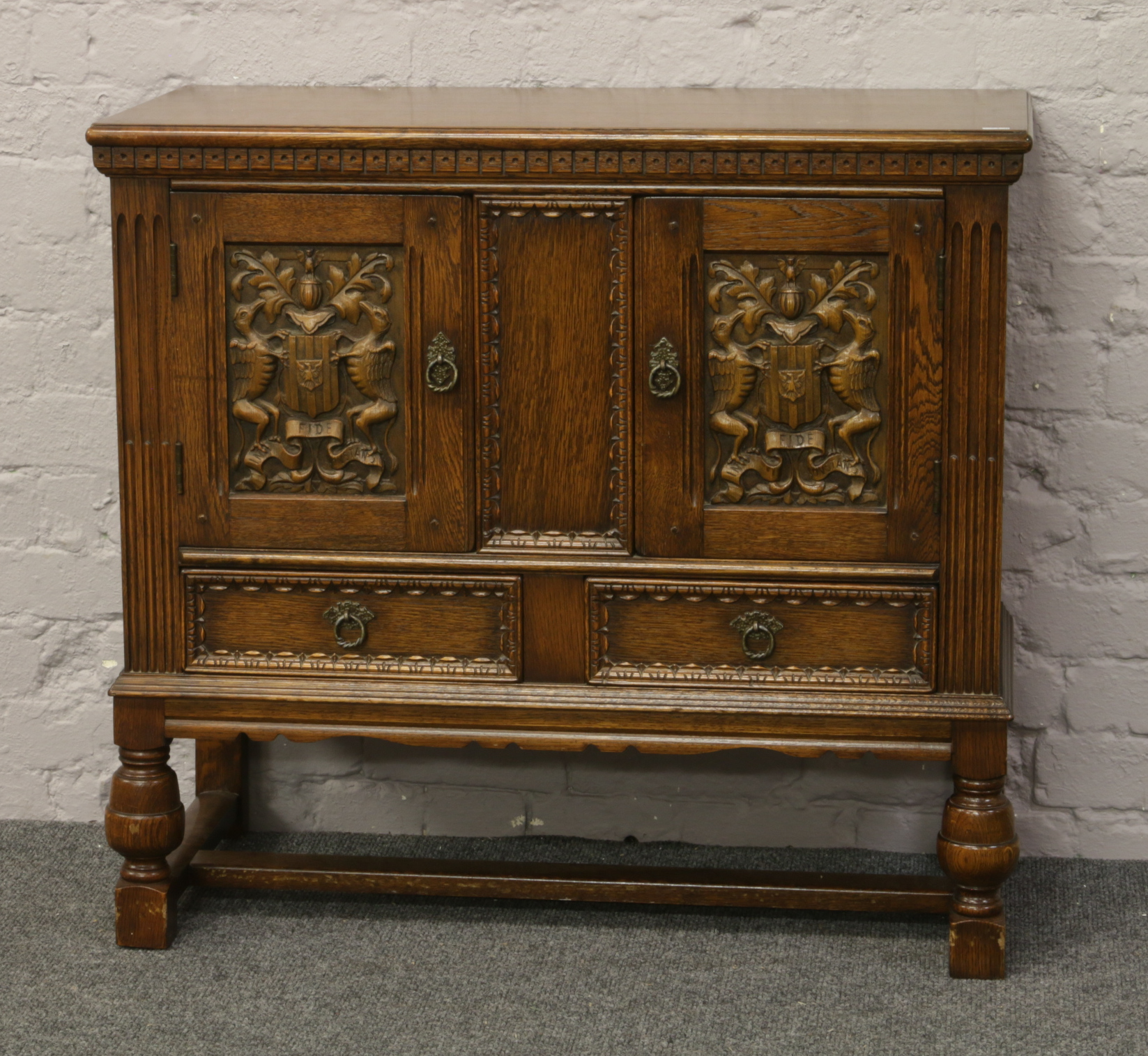 An Old Charm carved oak hutch cupboard with Heraldic panelled doors and raised over a H stretcher.