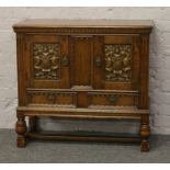 An Old Charm carved oak hutch cupboard with Heraldic panelled doors and raised over a H stretcher.