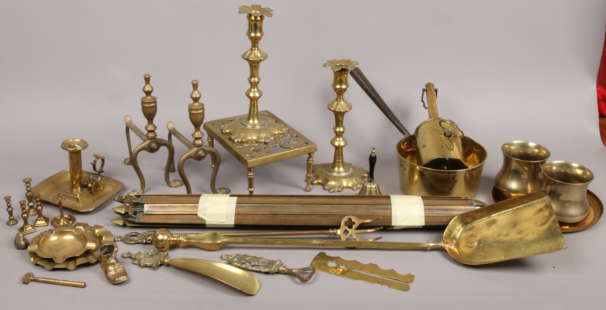 A collection of brassware to include Spitjack, candlesticks, firedogs, chamber stick and a bundle of