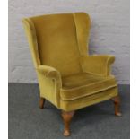 A wing back arm chair with mustard upholstery, raised on cabriole supports.