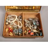 A vintage cigarette box containing 1950s costume jewellery including clip on earrings and