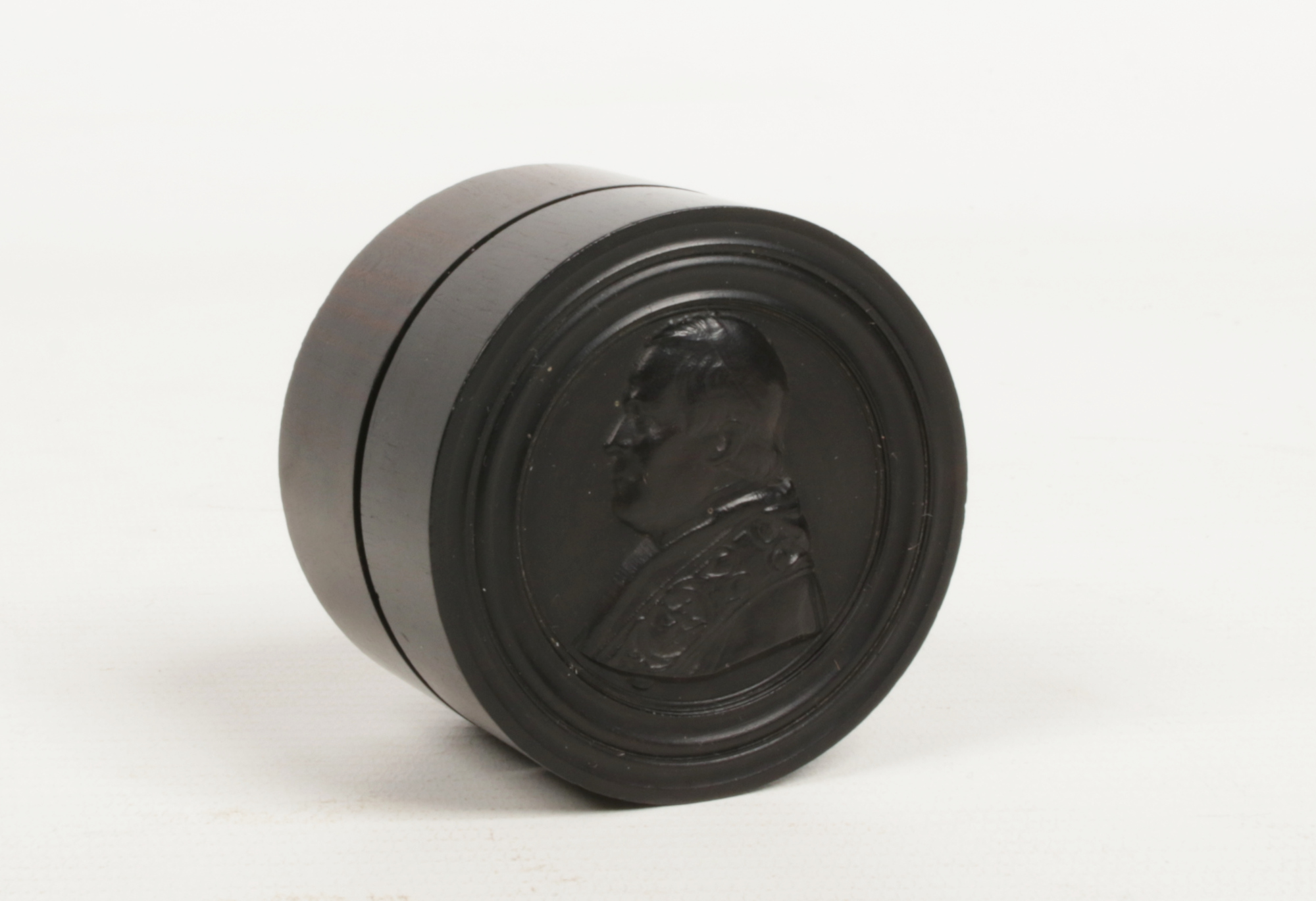 A hardwood cylindrical trinket box with threaded cover carved with a profile portrait of a pope,