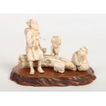 A Japanese Meiji period carved ivory figure group raised on a wooden plinth. Formed as a man