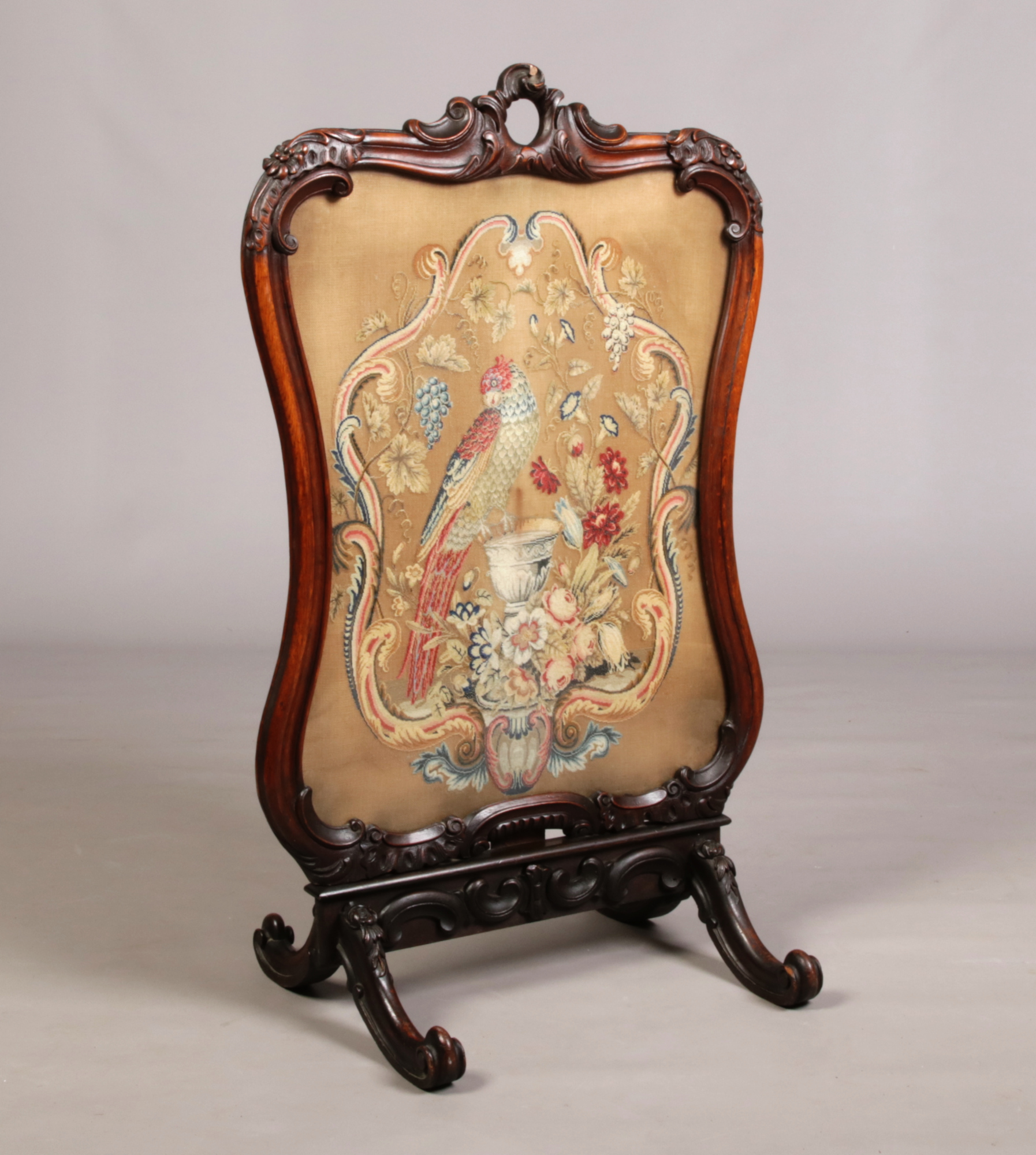 A large Victorian carved mahogany firescreen. With a needlework panel depicting a parrot and