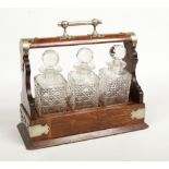 An Edwardian oak three bottle tantalus with silver plated mounts. Having rocking cradle and dated